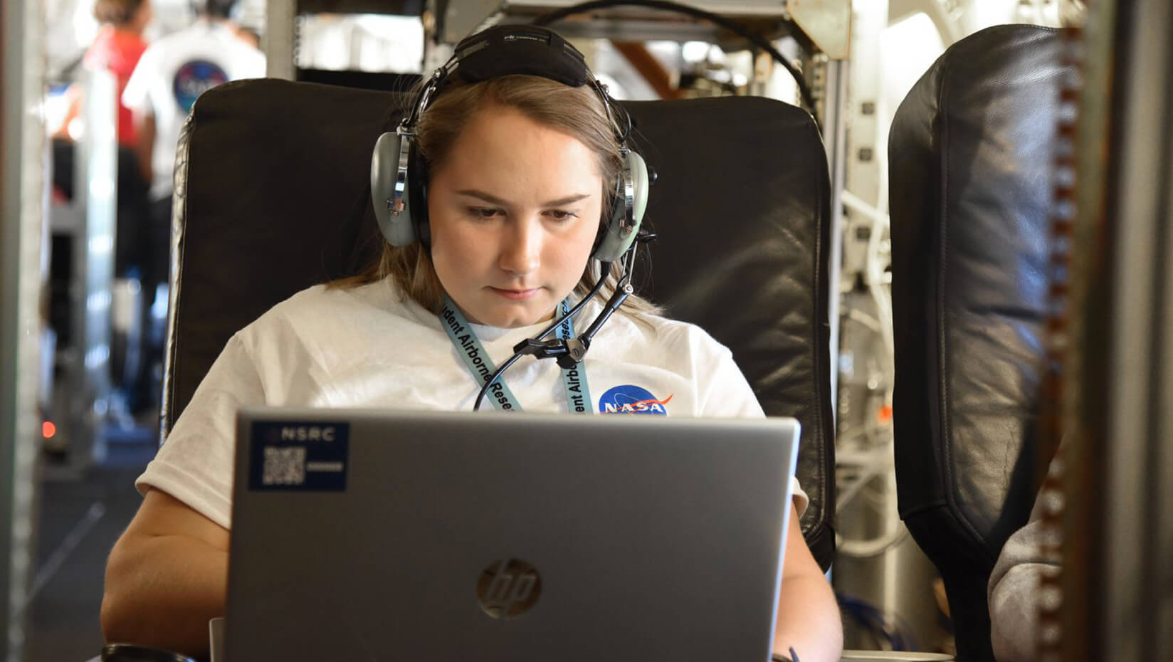 Honors student Laura Paye is shown wearing a headset, using a laptop, wearing a NASA tshirt