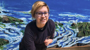 An image of Brynn Yarbrough standing in front of a painting of the ocean.