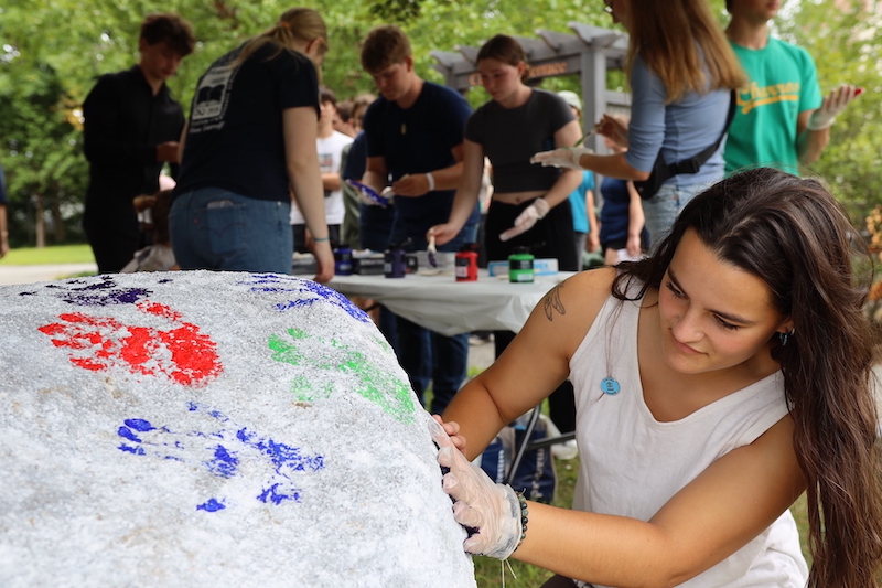 A student putting their handprint on a rock